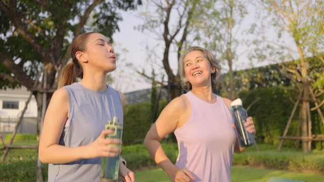 Young adult child workout outdoor public park run walk hold water bottle with mature middle age old mum. Love health care older mom asia elder people happy family protect aging fun joy city life sport