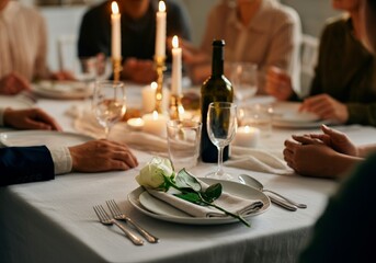 A family gathers around a candlelit dinner table in a moment of remembrance for the loss of a loved one. A single white rose on a plate on the table symbolizes the loved one being remembered.