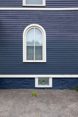 Fototapeta premium The exterior wooden wall of a vintage blue house with white painted trim. The building has three differently sized windows of various styles. The middle window is a half-round with four glass panes.