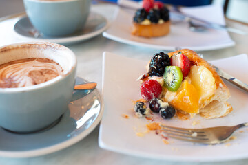 Two cups and saucers of hot cafe mocha. There's fruit pastries with blueberries, kiwi, strawberries, blackberries, peaches, and raspberries on top of custard fillings.