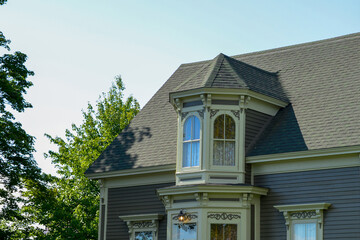 The top floor of a purple wooden historic house with cream-colored decorative trim. There are cross-gable peaked windows in the center of the roof. The vintage windows are arched with clear glass. 