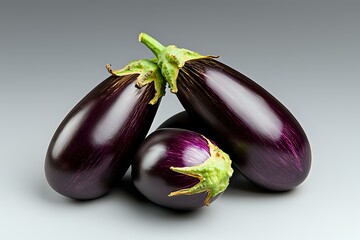 Fresh ripe eggplants with glossy purple skin and green stems on neutral background, close up view of organic vegetables for healthy cooking and nutrition.