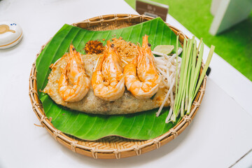 Pad Thai wrapped in an egg with shrimp on top in a plate made from Thai woven baskets.