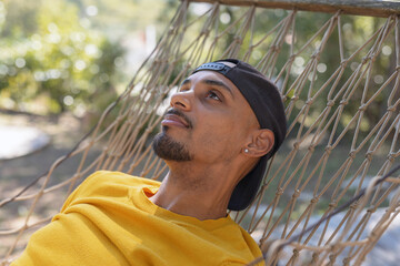 Young African American man enjoying the tranquility of nature, swaying and relaxing in a hammock....
