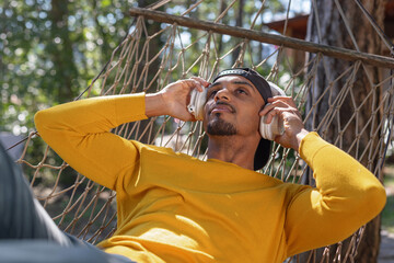 African American man enjoying nature outdoors, swaying and relaxing in a hammock listening to music on headphones.