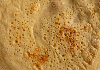 Surface Of Fried Pancake Dough With Tiny Holes. Yellow Background Of Baked Omelette Dough. Fresh Pancake Batter With Slightly Overcooked Spots.