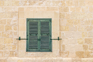 Traditional Maltese wooden window with green shutters in Valletta. A historic green shuttered window set in a limestone wall, reflecting Malta’s rich architectural heritage and Mediterranean character