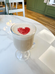 Glass cup of fresh hot aromatic cappuccino with latte art in shape of heart served on table.