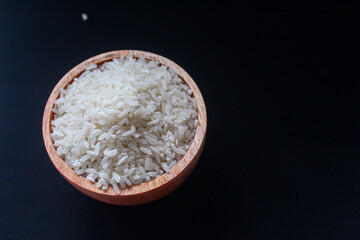 Zakat fitrah concept: Wooden bowl filled with rice on a black background.
