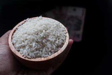 Zakat fitrah concept: hand holding a wooden bowl filled with rice to pay zakat fitrah, on a black background
