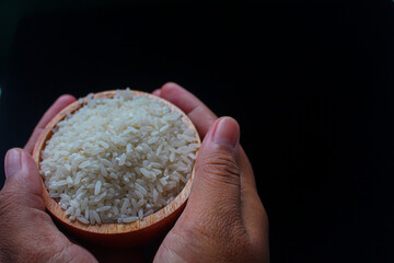 Zakat fitrah concept: hand holding a wooden bowl filled with rice to pay zakat fitrah, on a black background