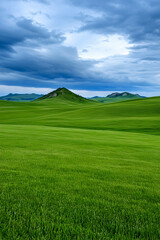 Fototapeta premium Lush green field under a dramatic sky, rolling hills in the distance