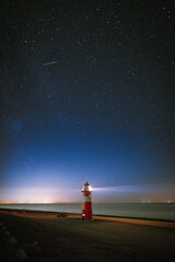 The Milky Way photographed at night with stars in the sky above a light beacon on the shor