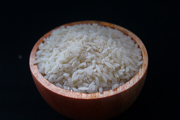 Zakat fitrah concept: Wooden bowl filled with rice on a black background.