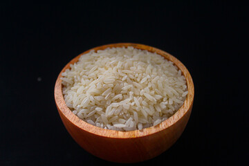 Zakat fitrah concept: Wooden bowl filled with rice on a black background.