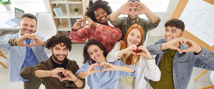 Team of happy smiling young diverse casual people business company coworkers together in office workplace looking up at camera, making hand hearts, showing love to customers. Banner, high angle, above