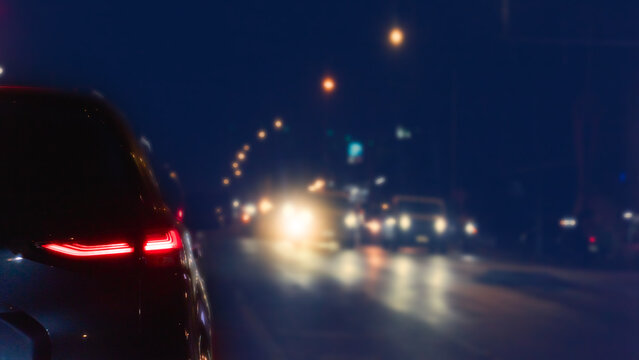 Abstract of nighttime scene of a car driving on a night road. The taillights of the car in the foreground are visible and the headlights of oncoming traffic are blurred in the distance. 