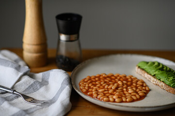 A homemade breakfast featuring avocado toast on whole grain bread, baked beans in tomato sauce,...