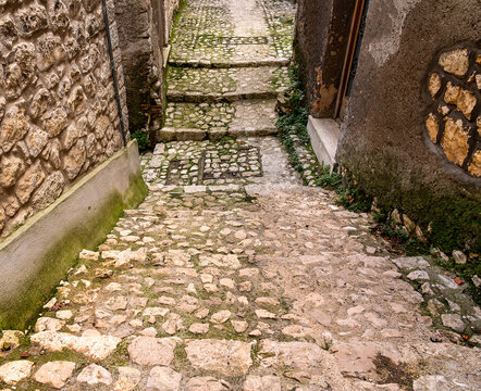 pedestrian alley with wide stone-covered steps downhill followed by steps uphill and flanked by stone walls partly with mould