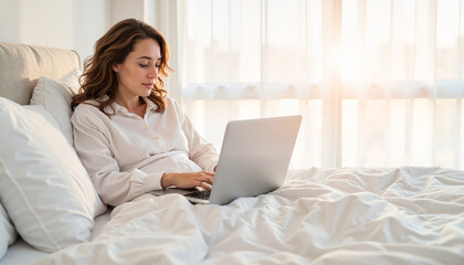 Naklejka premium Focused woman working on laptop in bed, morning routine