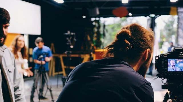 A behind-the-scenes view of a video shoot, featuring a close-up of a camera operator filming at eye level in a cozy, blurred background setting.