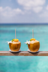 Tropical fresh coconut cocktail decorated with plumeria flowers on tropical resort water villa wooden deck. Perfect carefree travel closeup concept. Romantic couple honeymoon getaway, sunny blue sea