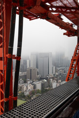 Fototapeta premium Looking through the framework of Tokyo Tower at the misty cityscape where towering buildings fade into dense fog while the industrial foreground adds depth and contrast