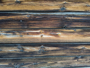 Powierzchnia ściany wykonanej ze starych desek zagruntowanych w przeszłości ciemnym podkładem. Część desek jest częściowo spruchniałych i pokrytych mchem. © boguslavus