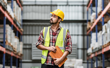 Asian handsome professional male worker holding board, checking shipping stocks in storage, warehouse or factory for delivery, wearing safety hat. Commercial Industry Business Concept.
