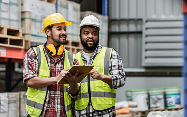 Two diverse professional male workers holding board, checking shipping stocks in storage, warehouse or factory for delivery, wearing safety hat. Diversity, Commercial Industry Business Concept.