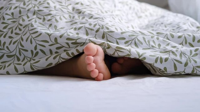 Barefoot. The child stuck his legs out from under the blanket, moved and hid them. A game of hide and seek. It got cold. Kid doesn't want to get up. Happy daytime sleep. Getting up to school concept.