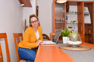 Young woman working from home using laptop at dining table