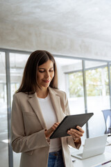 Fototapeta premium Vertical portrait of latin professional business woman working on computer at office workplace. Young businesswoman manager using pc tablet for sales management, financial operations or online banking