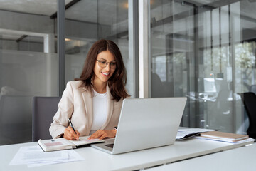 Middle-age latin woman using laptop computer for business studying, having videocall with online virtual webinar training meeting, writing notes. Focused businesswoman working in office. Copy space
