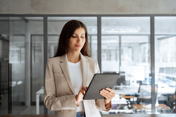Obraz premium Focused young specialist businesswoman manager using pc tablet for sales management, financial operations, online banking. Latin or middle eastern elegant business woman working on computer at office
