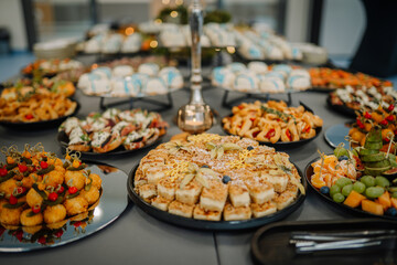 A festive table filled with assorted appetizers, fruits, pastries, and finger foods at a catered event, showcasing a colorful buffet arrangement..