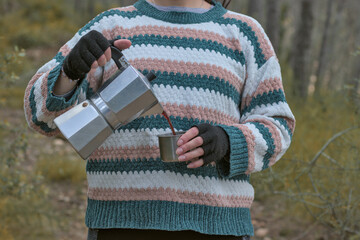 Woman with an Italian coffee maker and a thermal aluminum cup in the middle of a forest, woman camping drinking coffee