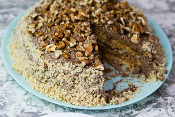 Delicious homemade cake with meringue, peanuts and walnuts on a light background. Sliced cake on a blue plate. Concept of natural homemade baking