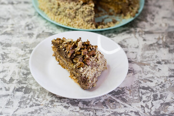 Delicious homemade cake with meringue, peanuts and walnuts on a light background. Appetizing piece of cake on a white plate close-up. Concept of natural homemade baking