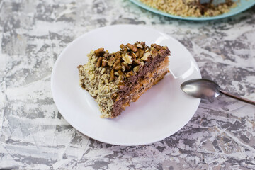 Delicious homemade cake with meringue, peanuts and walnuts on a light background. Appetizing piece of cake on a white plate close-up. Concept of natural homemade baking