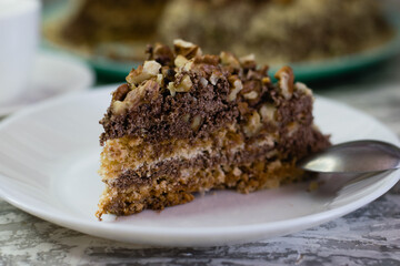 Delicious homemade cake with meringue, peanuts and walnuts on a light background. Appetizing piece of cake on a white plate close-up. Concept of natural homemade baking