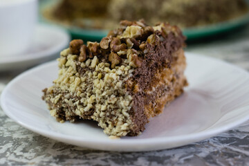 Delicious homemade cake with meringue, peanuts and walnuts on a light background. Appetizing piece of cake on a white plate close-up. Concept of natural homemade baking