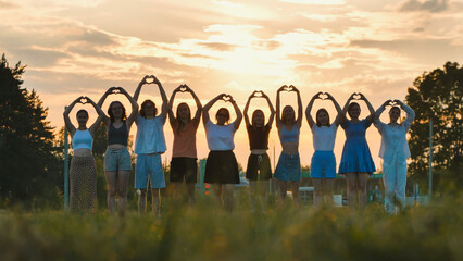 Fototapeta premium School friends forming a heart with their hands in front of a beautiful sunset, symbolizing friendship and unity