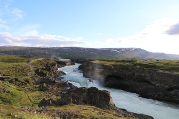 wild Skalfandafljot river running through a volcanic landscape with Godafosss waterfall in the distance cast in the soft light of the golden hour