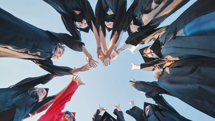 Graduates in academic gowns join hands in a circle, symbolizing unity, achievement, and the...