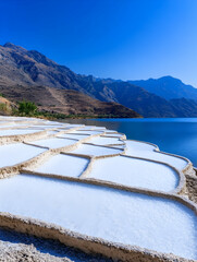 Serene terraced salt flats by a mountain lake under a clear blue sky