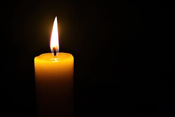 Single candle flame against dark background.  A solitary candle, warm yellow glow, casts a soft light in a black space
