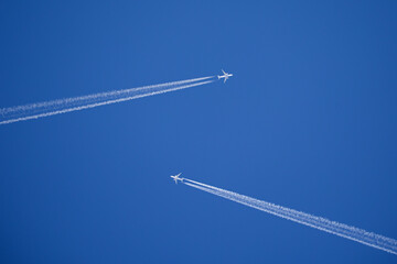 two white jets flying towards each other with long contrails in front of a blue sky