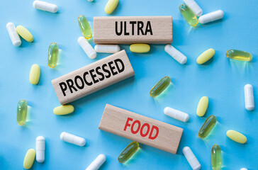 Medicine symbol. Concept words Ultra Processed Food on wooden blocks. Beautiful blue background with pills. Medicine concept and Ultra Processed Food. Copy space