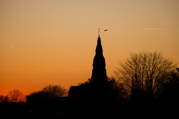 Sunset at the golden hour with the silhouette of the Christuskirche and a leafless tree in Ratingen Homberg with orange sky and airplane